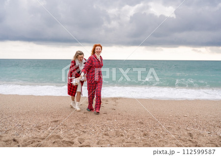 Sea two Lady in plaid shirt with a christmas tree in her hands enjoys beach. Coastal area. Christmas, New Year holidays concep Sea two Lady in plaid shirt with a christmas tree in her hands enjoys beach. Coastal area. Christmas, New Year holidays concep 112599587