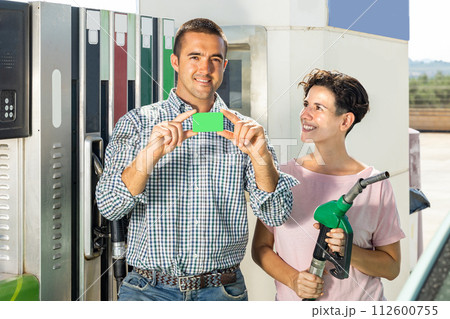 Smiling couple emonstrating gas credit card in gas station Smiling couple emonstrating gas credit card in gas station 112600755