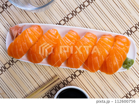 Blue rectangular ceramic plate of delicious salmon nigiri with soy souse on bamboo mat. 112600756