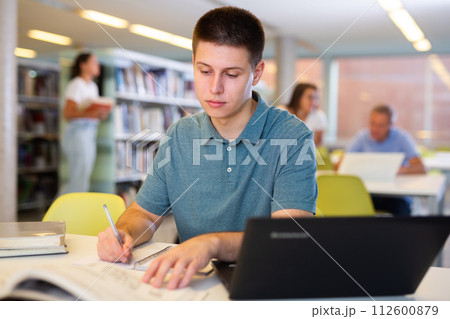 Young male student studying with a laptop in the library Young male student studying with a laptop in the library 112600879
