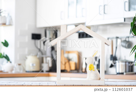 Key and tiny house of cozy home with Easter decor with rabbit and eggs on table of kitchen. Building, design, project, moving to new house, mortgage, insurance, rent and purchase real estate 112601037