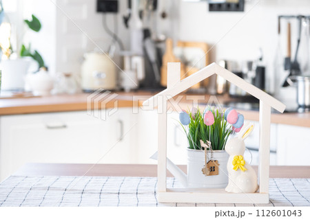 Key and tiny house of cozy home with Easter decor with rabbit and eggs on table of kitchen. Building, design, project, moving to new house, mortgage, insurance, rent and purchase real estate 112601043