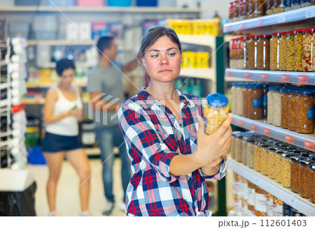 Young woman choosing canned beans in sauce in supermarket 112601403