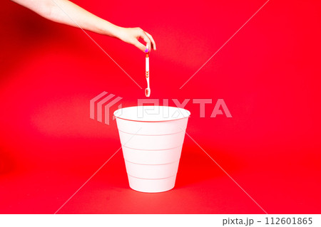 The toothbrush is thrown into the trash basket. Red background, copy space. The toothbrush is thrown into the trash basket. Red background, copy space. 112601865