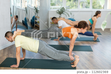 Young couple practicing acro yoga on mat with group of sporty people in yoga studio 112602369
