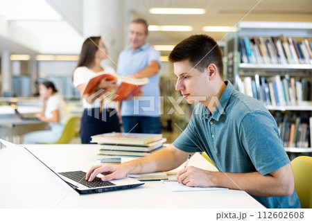 Concentrated young man checking plans in calendar while studying in the library and using laptop 112602608