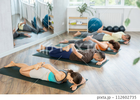 People doing back bending asana Dhanurasana, Bow Pose during group yoga workout in fitness studio 112602735
