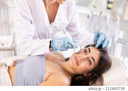 Young brunette undergoing high frequency ultrasound facial treatment 112602738