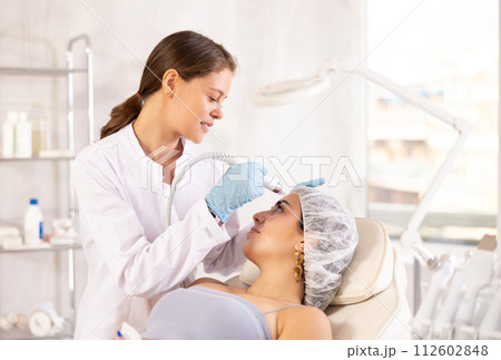 Aesthetician administering facial procedure on woman using ion bubble attachment 112602848
