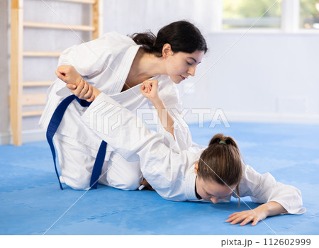 Sportive woman holds her opponent by force while sitting on mats during judo classes Sportive woman holds her opponent by force while sitting on mats during judo classes 112602999