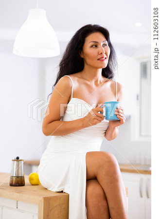 Attractive woman in nightgown drinking hot drink at home Attractive woman in nightgown drinking hot drink at home 112603108