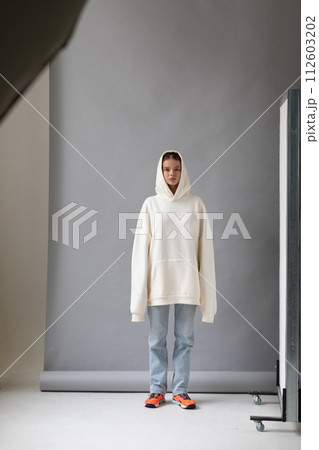 Beautiful blonde woman in a white hoodie and blue jeans posing on a gray background Beautiful blonde woman in a white hoodie and blue jeans posing on a gray background 112603202