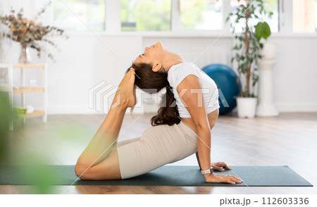 Young attractive woman practicing yoga, working out wearing sportswear, pants and top, in yoga studio Young attractive woman practicing yoga, working out wearing sportswear, pants and top, in yoga studio 112603336
