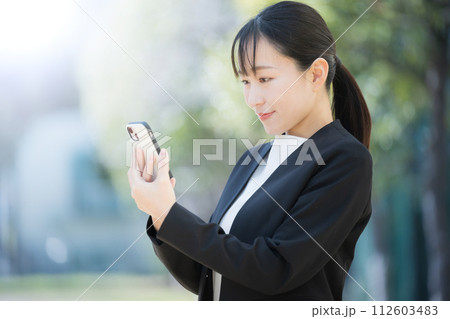 新緑の中、外でスマホを見る若いスーツの日本人(アジア人)女性 新緑の中、外でスマホを見る若いスーツの日本人(アジア人)女性 112603483