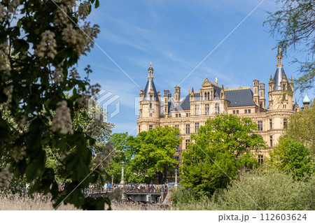 Schwerin Castle on Island in Schwerin Mecklenburg Vorpommern land Germany. Scenic view of historic german Schweriner palace with green garden against bright blue sky in Europe travel destination Schwerin Castle on Island in Schwerin Mecklenburg Vorpommern land Germany. Scenic view of historic german Schweriner palace with green garden against bright blue sky in Europe travel destination 112603624