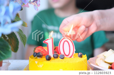 A person lighting a candle on a yellow cake with number 10 A person lighting a candle on a yellow cake with number 10 112603923