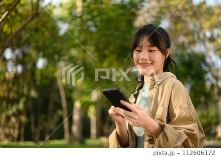 Attractive young woman sitting on bench in park and texting on her mobile phone 112606172