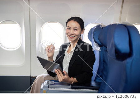 Smiling happy business woman asian flying and working in an airplane in first class, Woman sitting inside an airplane using digital tablet Smiling happy business woman asian flying and working in an airplane in first class, Woman sitting inside an airplane using digital tablet 112606735