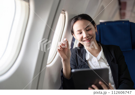 Smiling happy business woman asian flying and working in an airplane in first class, Woman sitting inside an airplane using digital tablet Smiling happy business woman asian flying and working in an airplane in first class, Woman sitting inside an airplane using digital tablet 112606747