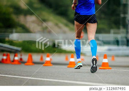 close up women legs running down road with orange safety cones, blue compression sleeves 112607491