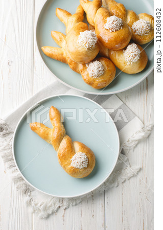 Easter bunny twist buns with coconut closeup on a plate on a wooden table. Vertical top view Easter bunny twist buns with coconut closeup on a plate on a wooden table. Vertical top view 112608432
