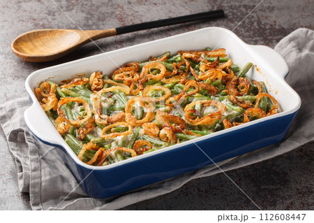 Green bean casserole with cheesy mushroom sauce and topped with crispy onions close-up in a baking dish. horizontal 112608447