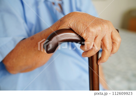 Asian elderly disability woman patient holding walking stick in wrinkled hand at hospital. 112609923