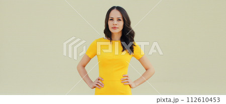 Beautiful young brunette woman model posing in yellow dress on city street Beautiful young brunette woman model posing in yellow dress on city street 112610453