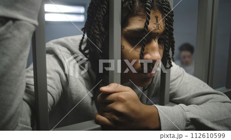 Close up shot of angry African American teenage prisoner in prison cell Close up shot of angry African American teenage prisoner in prison cell 112610599