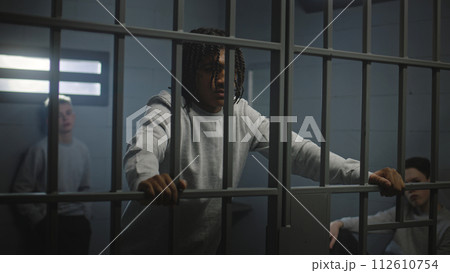 Multiethnic teenagers behind metal bars in prison cell look at camera 112610754