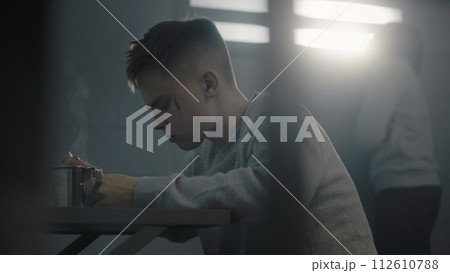 Caucasian teenage prisoner eats prison food at the table 112610788