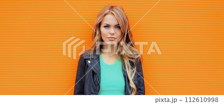 Portrait beautiful young blonde woman posing in black leather jacket on colorful orange background 112610998