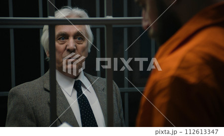 Lawyer talks with inmate standing in prison cell, offers his services 112613347