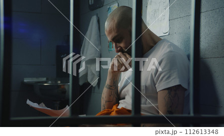 Male prisoner looks at his child drawings and cries sitting on bed in prison cell Male prisoner looks at his child drawings and cries sitting on bed in prison cell 112613348