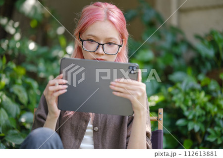 Cute pink hair girl drawing on digital tablet in garden, Woman Doing Freelance Work in Garden, woman with digital tablet with artwork. 112613881