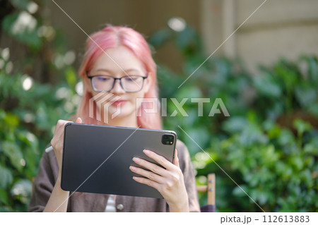 Cute pink hair girl drawing on digital tablet in garden, Woman Doing Freelance Work in Garden, woman with digital tablet with artwork. 112613883