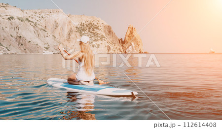Woman sea sup. Close up portrait of happy young caucasian woman with long hair looking at camera and smiling. Cute woman portrait in bikini posing on sup board in the sea 112614408
