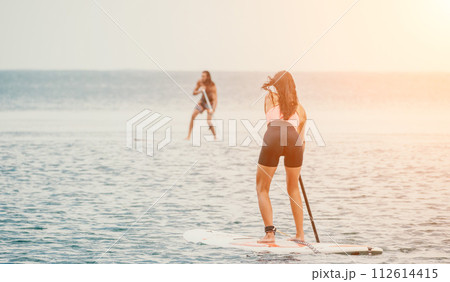 Sea woman and man on sup. Silhouette of happy young woman and man, surfing on SUP board, confident paddling through water surface. Idyllic sunset. Active lifestyle at sea or river. Sea woman and man on sup. Silhouette of happy young woman and man, surfing on SUP board, confident paddling through water surface. Idyllic sunset. Active lifestyle at sea or river. 112614415