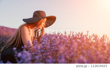 Woman lavender field. Happy carefree woman in black dress and hat with large brim smelling a blooming lavender on sunset. Perfect for inspirational and warm concepts in travel and wanderlust. Close up Woman lavender field. Happy carefree woman in black dress and hat with large brim smelling a blooming lavender on sunset. Perfect for inspirational and warm concepts in travel and wanderlust. Close up 112614425