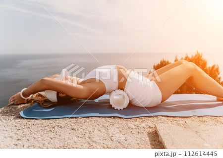 Fitness woman sea. Outdoor workout on yoga mat roller in park near to ocean beach. Female fitness pilates yoga routine concept. Healthy lifestyle. Happy fit woman exercising with rubber band in park. 112614445