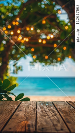 Empty wooden planks table against a blurred background with a sea coast with palm trees and glowing light bulbs in the evening 112617668