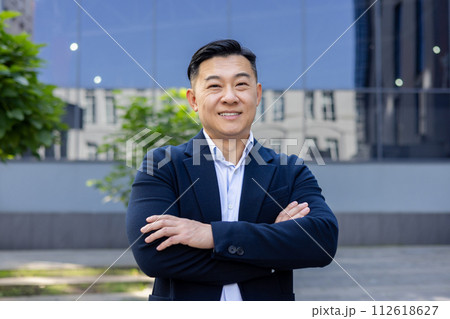 A professional businessman in a suit stands confidently with crossed arms in front of a modern office building, embodying corporate success. A professional businessman in a suit stands confidently with crossed arms in front of a modern office building, embodying corporate success. 112618627