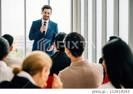 A diverse audience of colleagues sits and attentively listens as business leaders present their reviews in a meeting room. This embodies the essence of teamwork and the success it brings. 112619283
