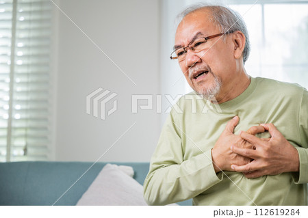 Sad senior man feeling bad pain use hand touching chest having heart attack on sofa in living room, Worried Asian old man have congenital disease suffering from heartache alone at home his heart aches 112619284