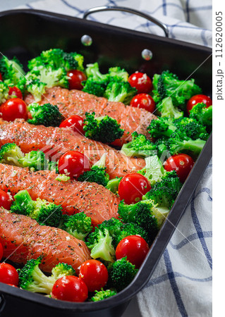Raw salmon fillet with broccoli and tomato on frying tray, ready to bake, vertical 112620005