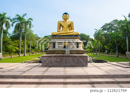 An iconic golden Buddha statue in Viharamahadevi Park a public park located in Colombo, Sri Lanka. Viharamahadevi park is the oldest and largest park of the Port of Colombo. 112621794