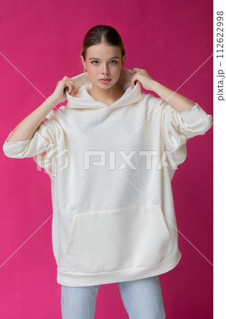 Beautiful blonde woman in a white hoodie and blue jeans posing on a pink background Beautiful blonde woman in a white hoodie and blue jeans posing on a pink background 112622998