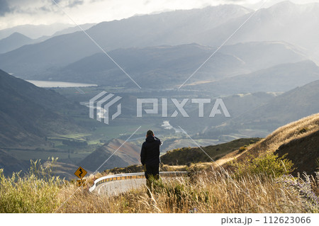 Man taking photograph of beautiful river valley surrounded by mountains with his phone, New Zealand Man taking photograph of beautiful river valley surrounded by mountains with his phone, New Zealand 112623066