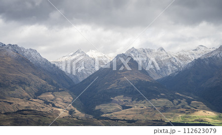 View on snowy mountains rising from green pastures during overcast cloudy day, New Zealand 112623079