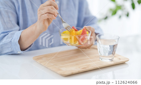 水のグラスを手にフルーツを食べるミドル女性の手元 水のグラスを手にフルーツを食べるミドル女性の手元 112624066
